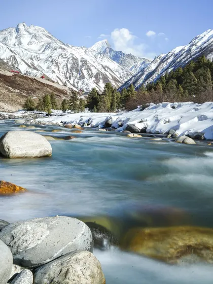 A series of photos capturing the serene beauty of a river flowing through a snow-lined valley. The long-exposure shot creates a milky effect on the water, contrasting with the sharp peaks.