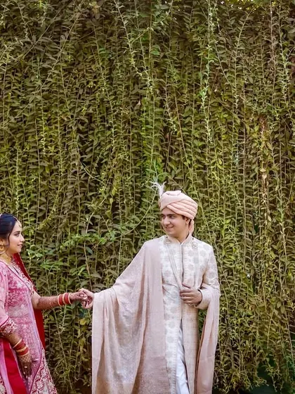 A beautiful, wide-angle shot of the couple against a wall of lush greenery. The groom gently leads his bride, creating a sense of a shared journey beginning.