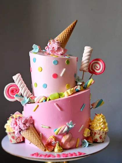 A slightly angled view of the pink topsy-turvy cake, highlighting the tilted tiers and the arrangement of lollipops and marshmallows.