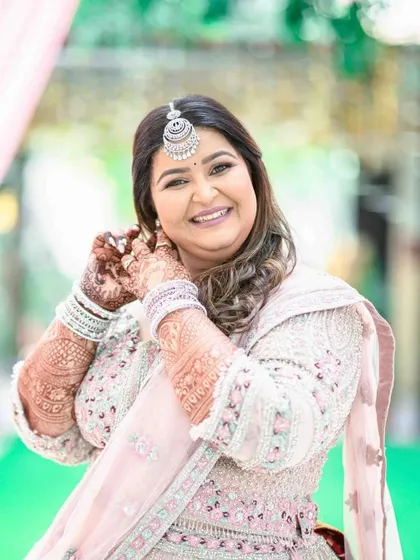A happy bride in a pastel pink lehenga. The makeup is soft and luminous, perfect for a daytime event.