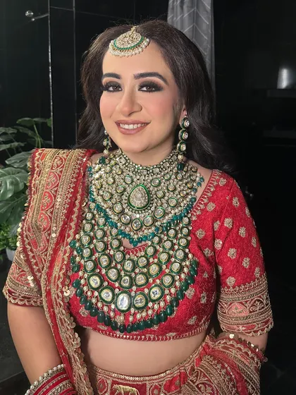 A happy Sabyasachi bride on her wedding day. Her look features soft, wavy hair and a radiant makeup look with a focus on glowing skin and beautifully defined eyes, paired with a magnificent emerald necklace.