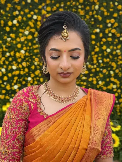 A close-up of the bride against a wall of flowers. The soft, shimmering eye makeup and flawless skin create a look that is both romantic and timeless.