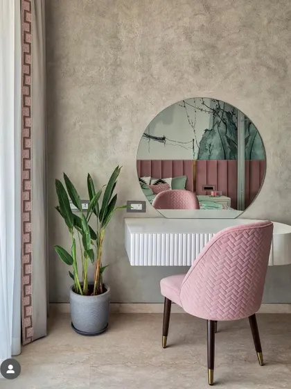 A minimal dressing unit in a bedroom, featuring a floating white console, a round mirror, and a plush pink chair. The textured grey wall provides a calm and sophisticated backdrop.