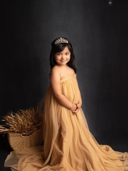 A beautiful, classic portrait of a five-year-old princess. Her sweet smile and the elegant golden gown shine against the dark, dramatic background.