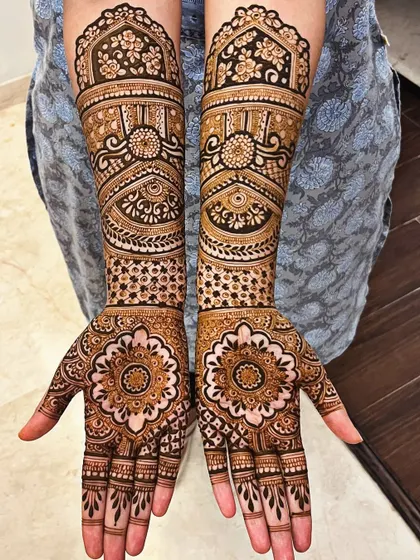 This design is centered around a detailed mandala on the palm, a symbol of the universe and wholeness. The arms are decorated with matching floral and architectural patterns for a cohesive bridal look.