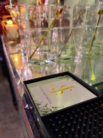 A custom coaster with the event hashtag #sanjtookthedive, placed neatly on the bar mat. It's a functional detail that also encourages social sharing.