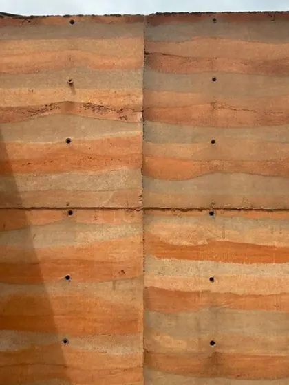 Another view of the panelled rammed earth wall, with sunlight highlighting its wavy, sedimentary-like layers.