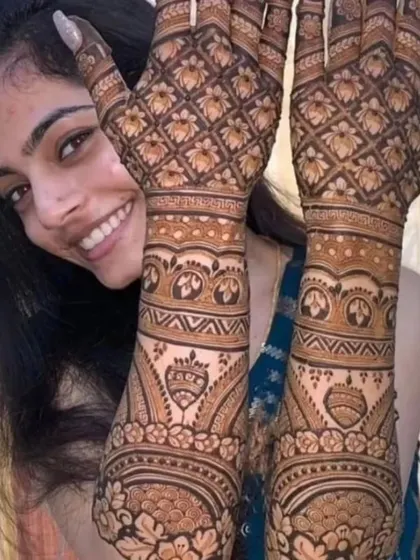 A happy bride peeking through her hands, which are adorned with a beautiful lotus and geometric pattern mehendi.