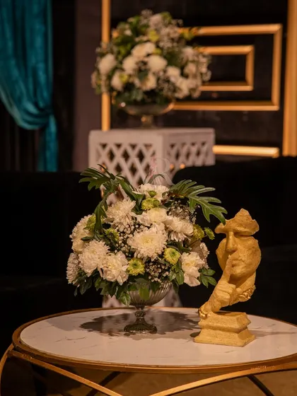 A small, artistic detail on a coffee table. A cherub-like sculpture stands next to a simple arrangement of white carnations, adding a touch of classical art to the modern lounge.