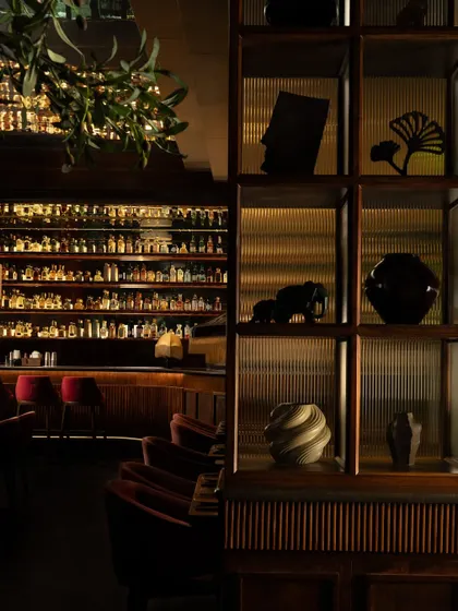 A view towards the bar at Hikki, framed by shelving filled with curated artifacts. The fluted glass and warm backlighting create a sense of depth and intrigue, highlighting the meticulous attention to detail in this hospitality design.