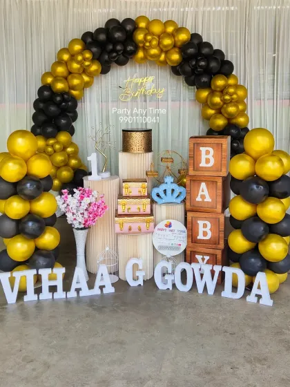 A classic first birthday setup with black and gold balloons, "BABY" blocks, and large letters for the name.