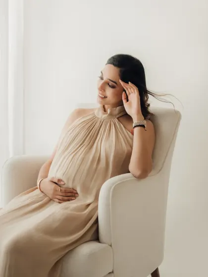 A close up shot showing the beautiful texture of this beige halter gown. A gentle smile and a hand on the bump create a classic and peaceful maternity portrait.