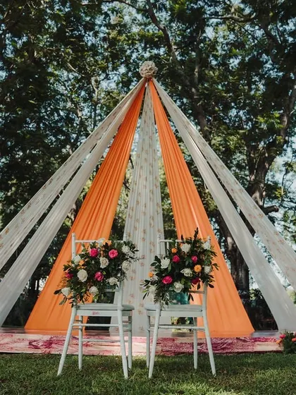 A modern and chic teepee-style mandap with orange and white drapes, perfect for a contemporary outdoor wedding ceremony.
