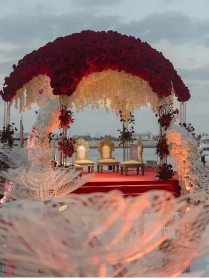A closer look at the floating mandap design. The rich red roses on the canopy contrast beautifully with the hanging white flowers, perfect for a romantic and luxurious waterside wedding.