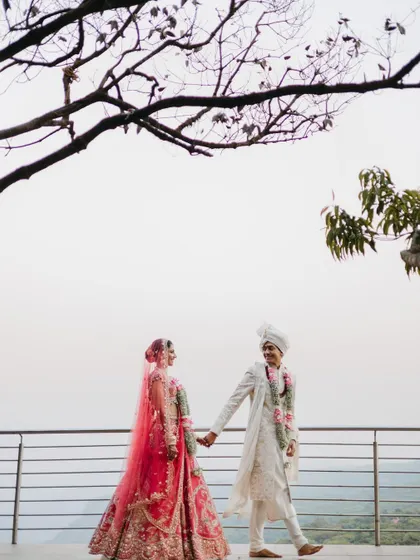 A romantic portrait of a couple walking hand-in-hand on a balcony, their traditional wedding attire complementing the scenic backdrop.