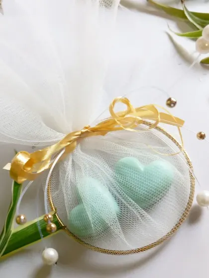 A close-up view of the handcrafted wedding favor, showing the detail of the golden ribbon and the delicate heart-shaped wax melts nestled inside.