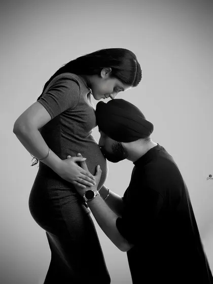 A tender and intimate black and white portrait. The dad-to-be gently kisses the baby bump, creating a powerful and emotional image of love and connection.