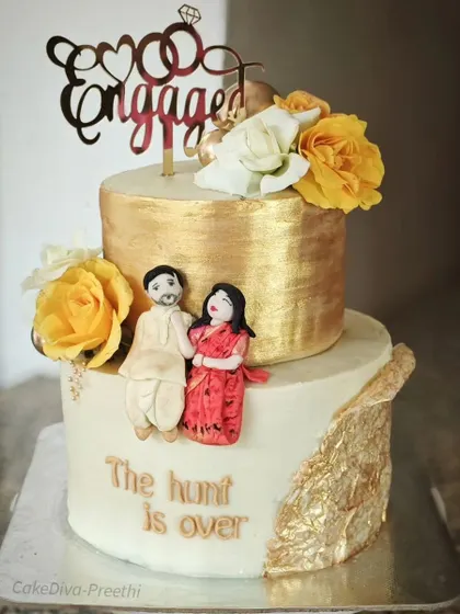 "The hunt is over!" This stunning two-tier engagement cake is decorated with gold leaf, fresh flowers, and a personalized fondant couple. It's a delicious butter chocolate sponge with hazelnut filling.