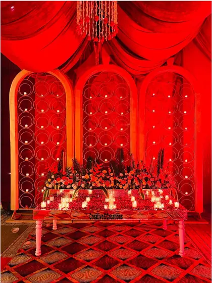 A stunningly lit table setup in all red. The backdrop with arched panels and the candle-lit table create a dramatic and romantic atmosphere.
