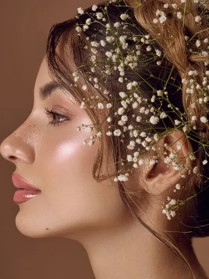 A profile view of the floral hair concept. This angle highlights the delicate baby's breath woven into the braid and the beautiful, dewy highlight on the model's cheekbone.