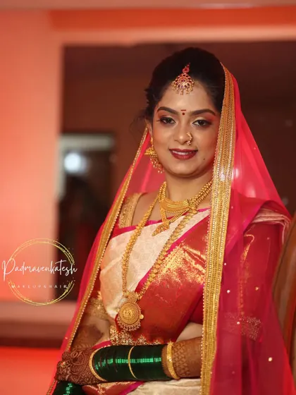 A classic muhurtham look featuring a beautiful red and white saree. The makeup is kept traditional with gold-toned eyes, a red bindi, and a bold lip, perfectly capturing the essence of a South Indian wedding.