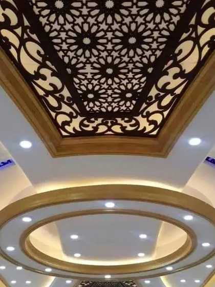 A grand ceiling that combines a circular recessed section with a large, ornate jali panel. The mix of spotlights and cove lighting creates a bright and luxurious space.