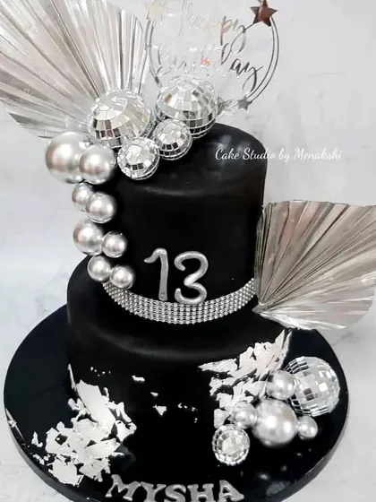 A glamorous black and silver disco party cake for a 13th birthday. This two-tier cake is decorated with disco balls, silver leaf, and sparkling rhinestones.