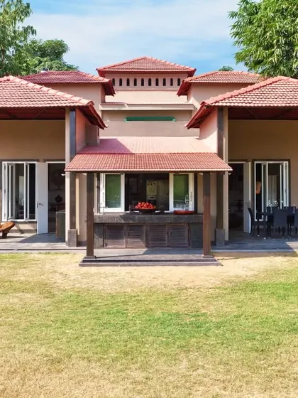 The front facade of the Aishbagh cottage, showcasing its symmetrical design and layered, sloped roofs with terracotta tiles. The architecture is designed to feel organic and rooted in its natural environment.