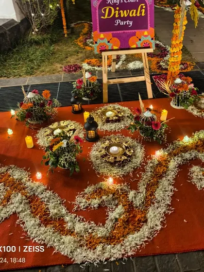 An intricate flower rangoli design made with marigold and rose petals, with diyas and lanterns, for a Diwali party entrance.