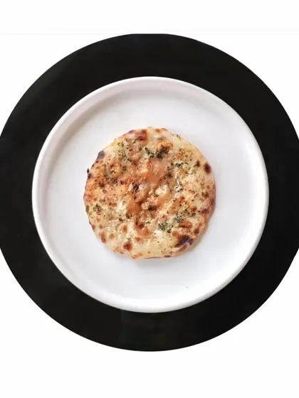 A simple, perfectly baked naan, presented on a white plate against a black background. Your journey at Indian Accent is incomplete without our breads.