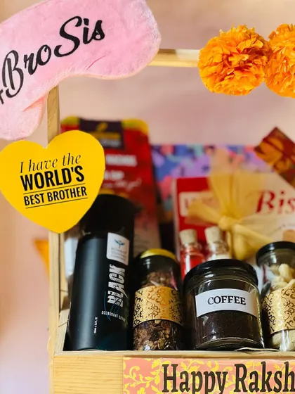 A close-up of a two-tiered Rakhi hamper for a brother, featuring a "#BroSis" eye mask and a "World's Best Brother" tag.