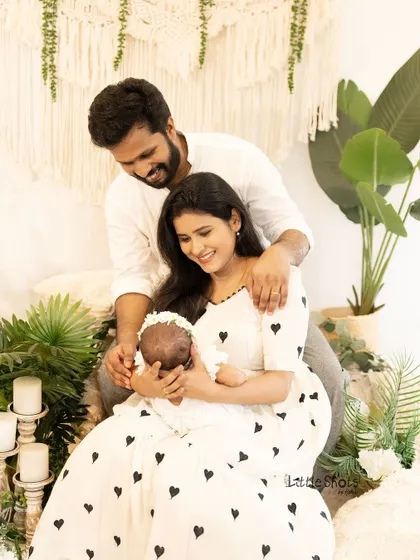 A candid and joyful moment with a new baby. The parents are all smiles as they cradle their newborn in a bright, boho-inspired studio setting.