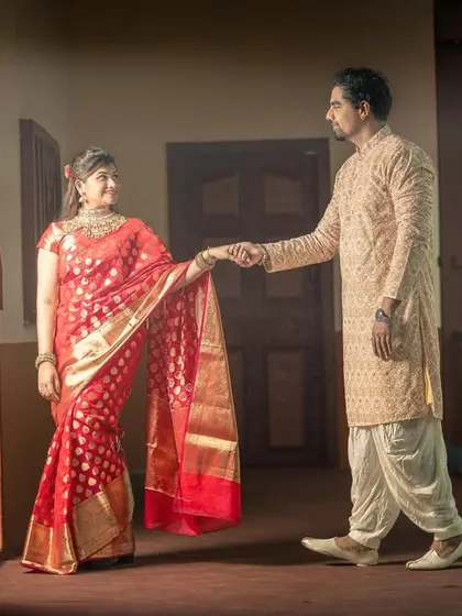 A romantic shot inside a traditional home, where the groom gently leads the bride, showcasing the beauty of her red and gold saree.
