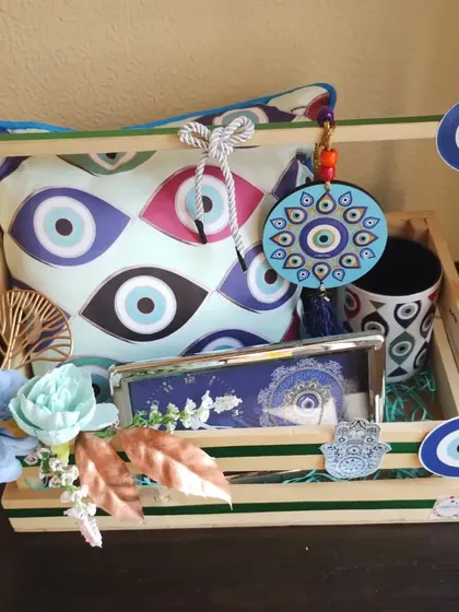 An evil eye themed hamper filled with home decor items. It includes a printed cushion, a matching mug, a hanging charm, and a table clock.