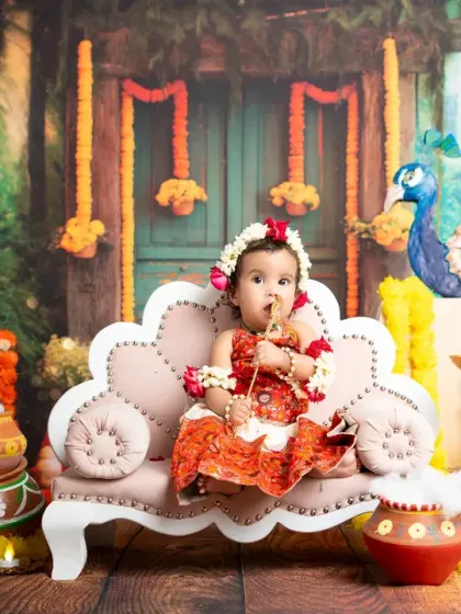 A sweet baby girl dressed as a Gopi for Janmashtami, sitting on a divan amidst a festive setup. These themed shoots are perfect for celebrating cultural festivals.