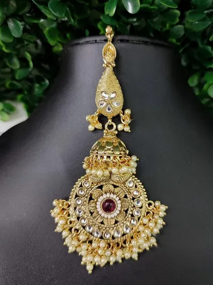 An oversized passa-style maang tikka with a central ruby stone. The intricate design and pearl drops make it a statement piece.