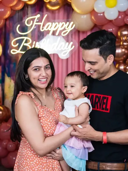 A happy family of three celebrating their daughter's first birthday. The neon "Happy Birthday" sign and the beautiful balloon arch create a modern and festive party vibe.
