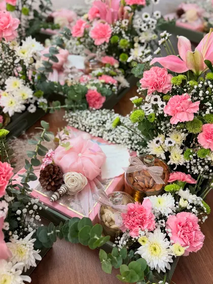 An array of our bespoke Roka favors, featuring fresh pink and white flowers. Each gift set includes a beautifully wrapped box and jars of premium dry fruits, creating a lush and celebratory display.