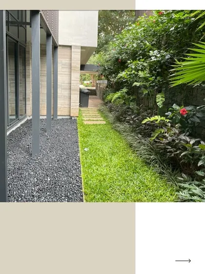 This narrow side yard of a villa is transformed with a mix of textures. A clean grass path is flanked by a modern pebble bed on one side and a lush border of tropical plants on the other, making the most of a compact space.