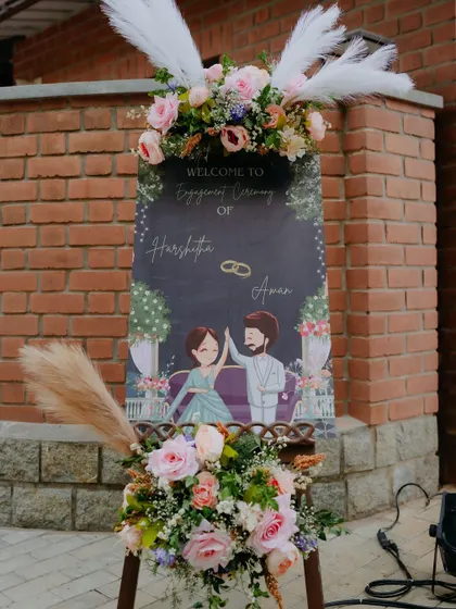 A personalized engagement welcome sign featuring a cute caricature of the couple, adorned with pampas grass and roses.