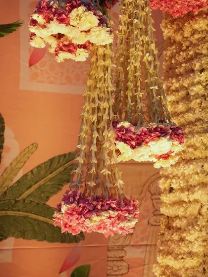 A close-up of the hanging floral chandeliers, crafted from strings of tuberose and accented with rings of pink and white carnations. These delicate structures add a touch of grace and movement.