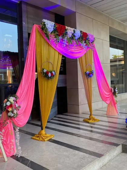 A vibrant entrance decoration with yellow and pink drapes. The hanging floral baskets add an extra decorative element.