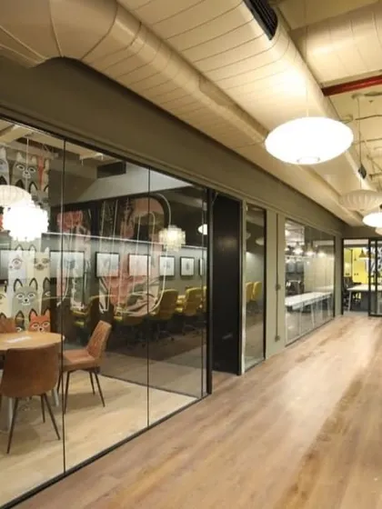 A corridor at an Innov8 coworking space, showing a glass-walled meeting room with quirky wallpaper on one side and a long counter with yellow chairs for focused work on the other.