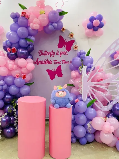 A beautiful butterfly-themed third birthday party. The setup features a purple and pink balloon arch on a custom backdrop.