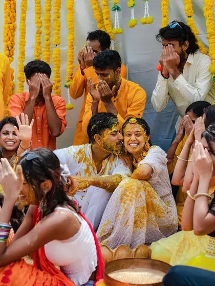 A candid moment of friends and family reacting with laughter and joy during a messy and fun Haldi ceremony.