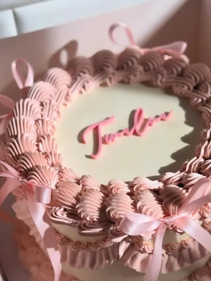 This vintage-style cake, with its dusty pink buttercream ruffles and delicate ribbons, is boxed up and ready for a celebration. The personalized name adds a final, sweet touch.