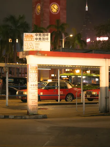 A red taxi at a bus stop in Hong Kong at night, with the historic clock tower in the background. Night photography allows me to play with artificial light sources to create a dramatic mood.