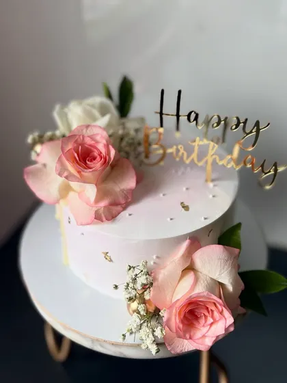 A delicate pink birthday cake adorned with fresh roses and baby's breath. The scattered gold leaf adds a touch of sparkle to this beautiful design.