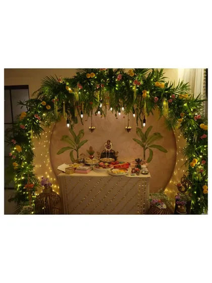 We designed this breathtaking Ganpati mandap, creating a divine focal point for the celebration. The setup features a lush arch of fresh palm leaves and florals, warmly lit by fairy lights and hanging Edison bulbs, all framing a custom-painted backdrop for a truly serene atmosphere.