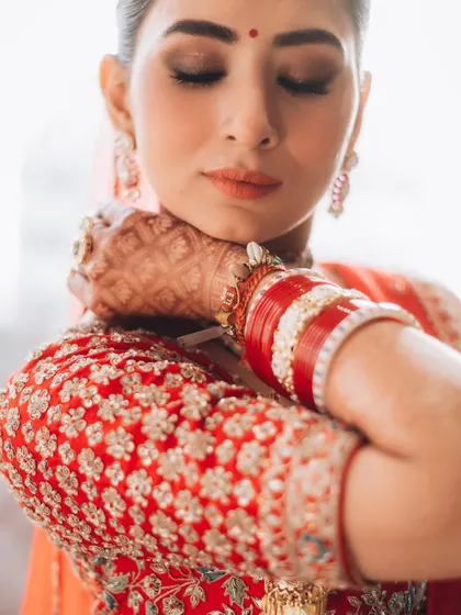 A serene moment as the bride gets ready. The focus on her traditional red and white bangles and the delicate embroidery of her blouse highlights key bridal details.